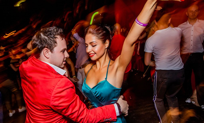 Woman dressed in blue dress dancing with man in red jacket