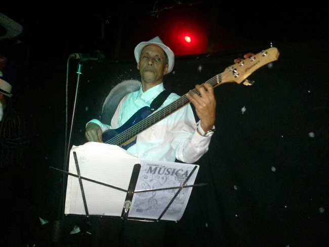 Pedro González dressed in white playing the bass